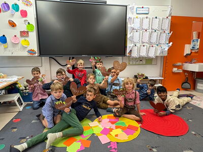 Schüler sitzen am Boden und halten braune Herzen mit lustigen Aufschriften hoch