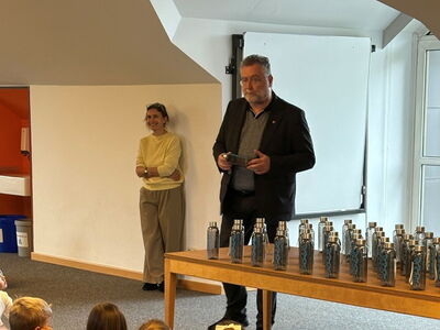 Bürgermeister steht vor den Schülern mit Trinkflaschen auf dem Tisch