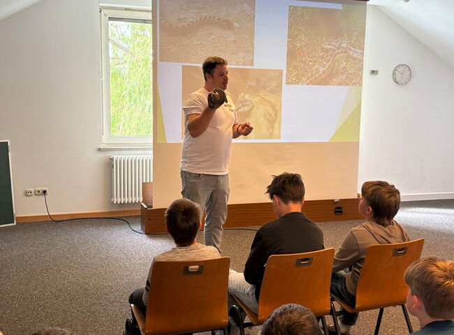 Tobias Lau steht mit einer kleinen Schlange in der Hand vor Schülern