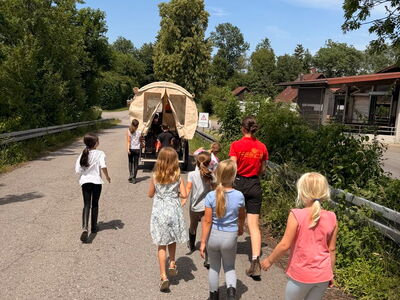 Kinder laufen hinter einem Planwagen her