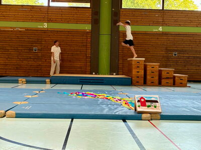 Ein Schüler springt in der Turnhalle von einem Kasten auf eine Matte
