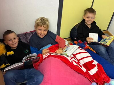 Drei fröhliche Schüler sitzen mit je einem Buch auf bequemen Sitzmöglichkeiten