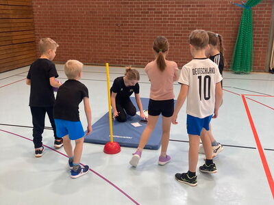 Schulkinder mit einer Trainerin an einer Matte in der Turnhalle