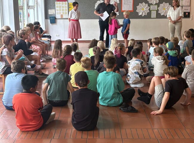 Bürgermeister gratuliert einer Gruppe von Schülern, welche am Boden im Kreis sitzt