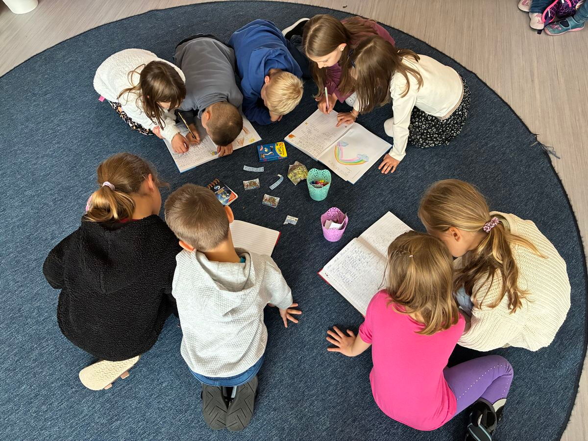 Kinder sitzen gemeinsam auf einem Teppich und nehmen Hefteinträge vor