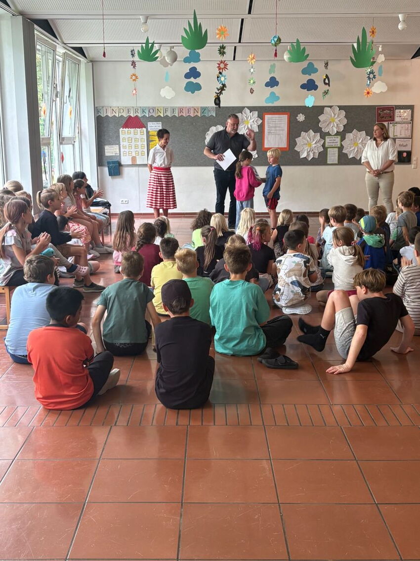Bürgermeister gratuliert einer Gruppe von Schülern, welche am Boden im Kreis sitzt