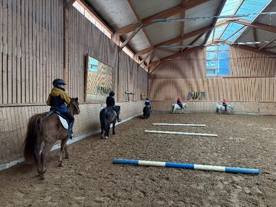 Kinder reiten auf Ponys in einer Reithalle